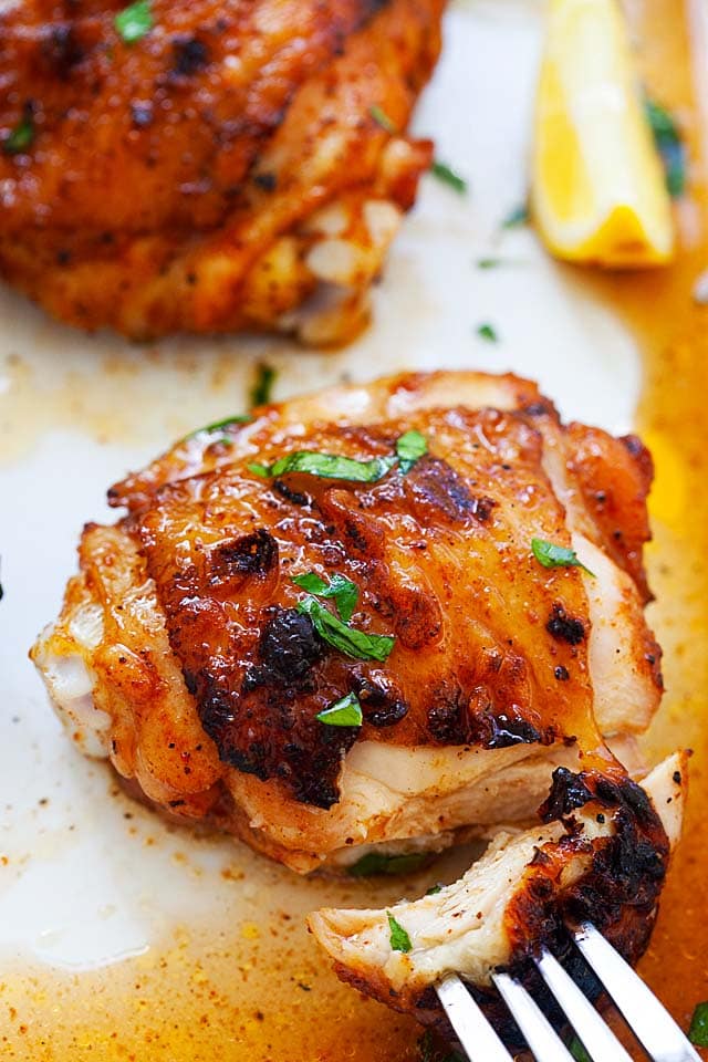 A piece of perfectly grilled and BBQ chicken thighs picked with a fork, with juice flowing out on the serving tray.
