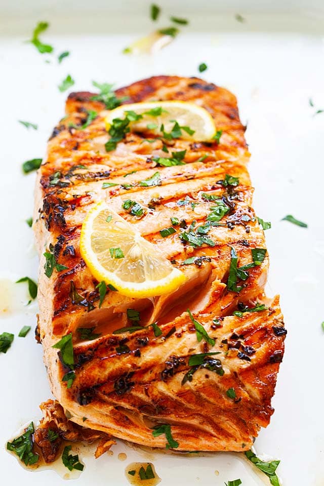 Healthy and best grilled salmon recipe with lemon, garlic, herbs and olive oil, with juice oozing out from the grilled salmon fillet.