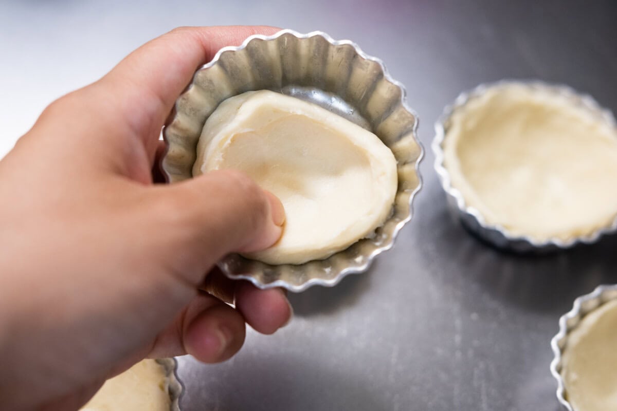 Puff pastry dough is pressed into an egg tart mold.