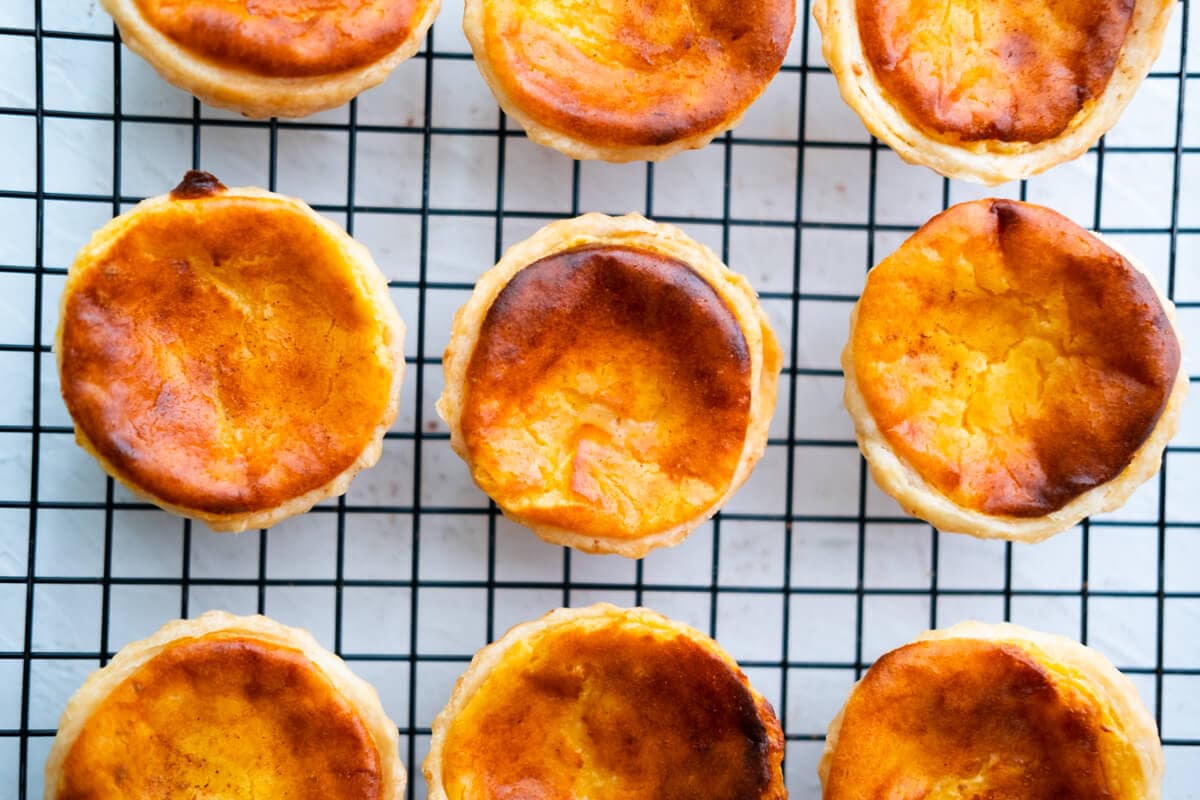 Golden brown Portuguese egg tarts on a wire rack. 