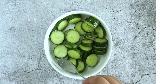 Putting salt in a bowl full of sliced cucumbers