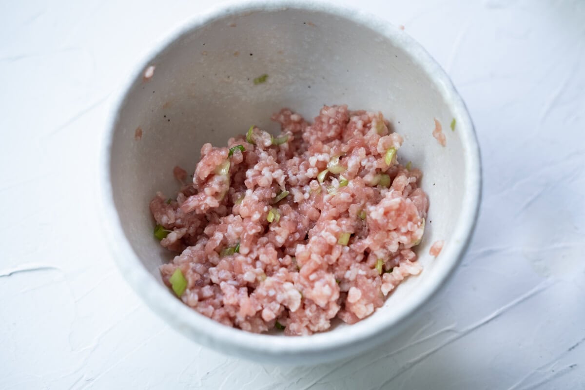 Ground pork seasoned with salt, white pepper, and chopped scallions in a small bowl. 