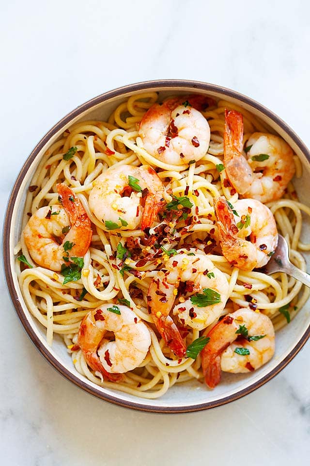 Spaghetti aglio e olio with shrimp, garnished with parsley and additional red pepper flakes. 