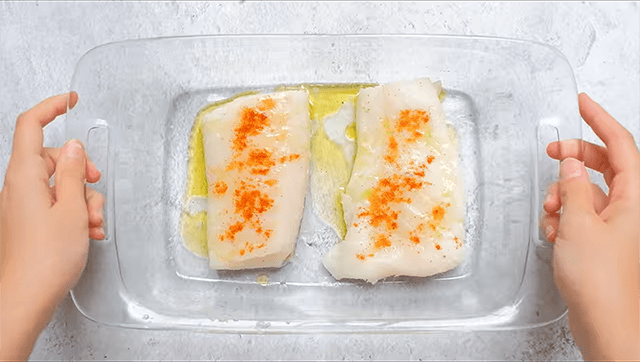 Raw cod fish fillets with lemon juice, salt and cayenne paper in a baking tray.