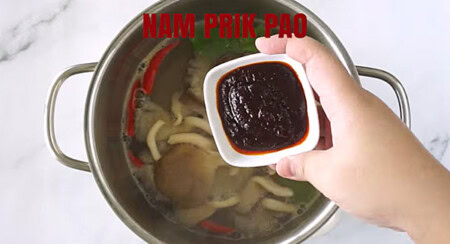 Adding nam prik pao or Thai roasted chili paste in the tom yum soup.