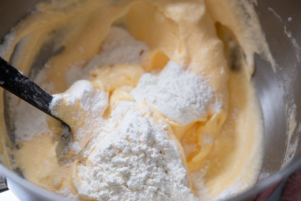 Adding egg yolks, sifted flour and fold gently in a bowl using a spatula. 