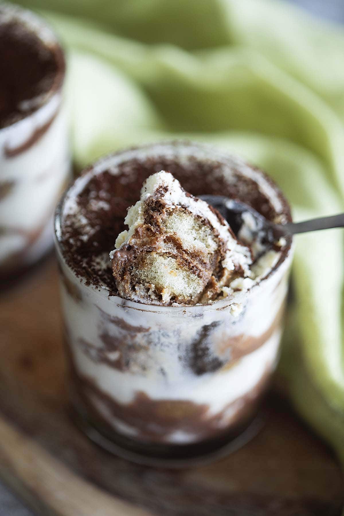 A spoon scooping out some eggless Tiramisu from a cup. 