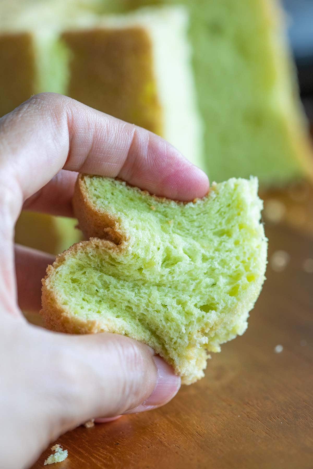 A person squishing a slice of pandan sponge cake showing its soft and airy texture. 