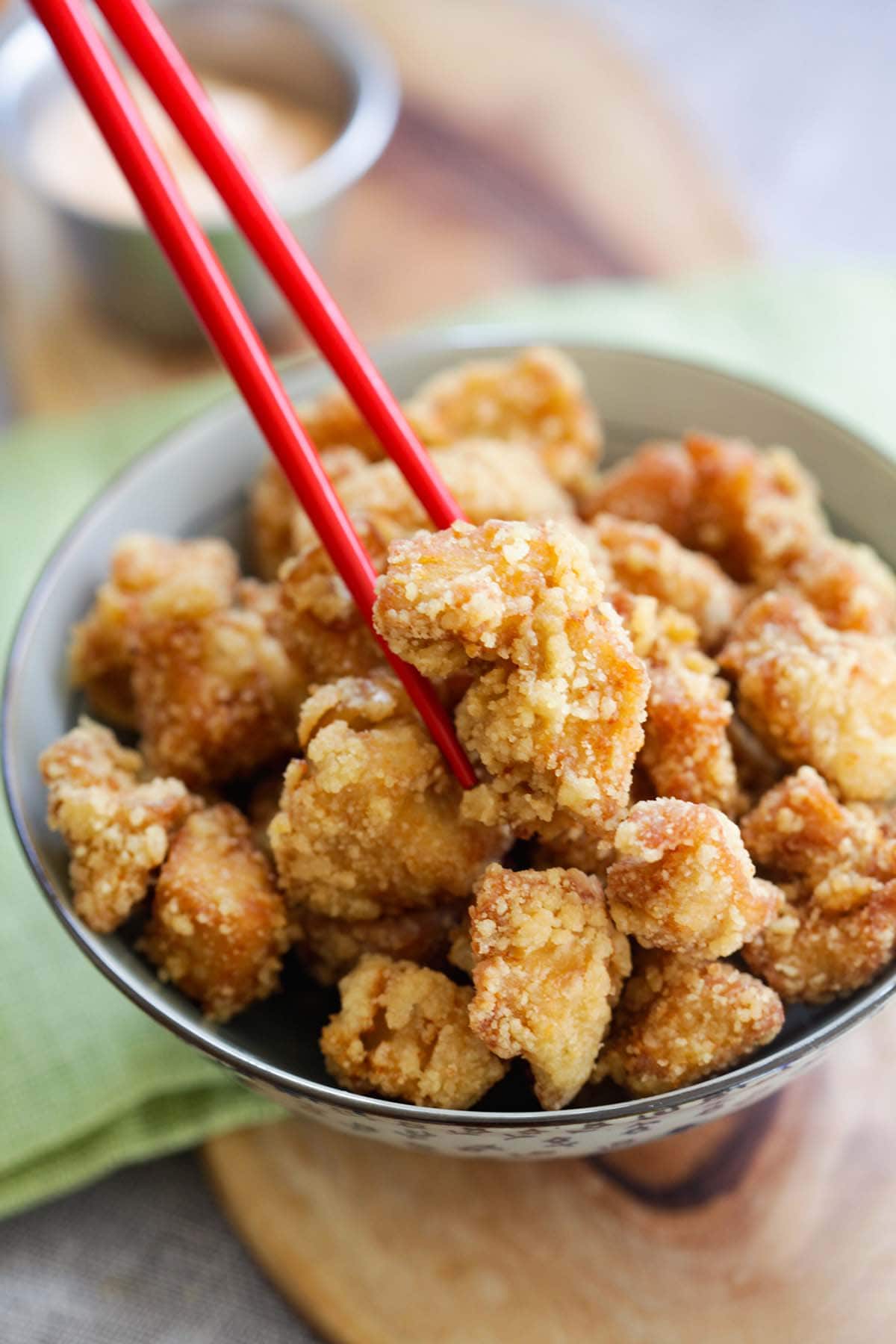 A pair of chopsticks picking up a piece of crispy chicken Karaage from a bowl.