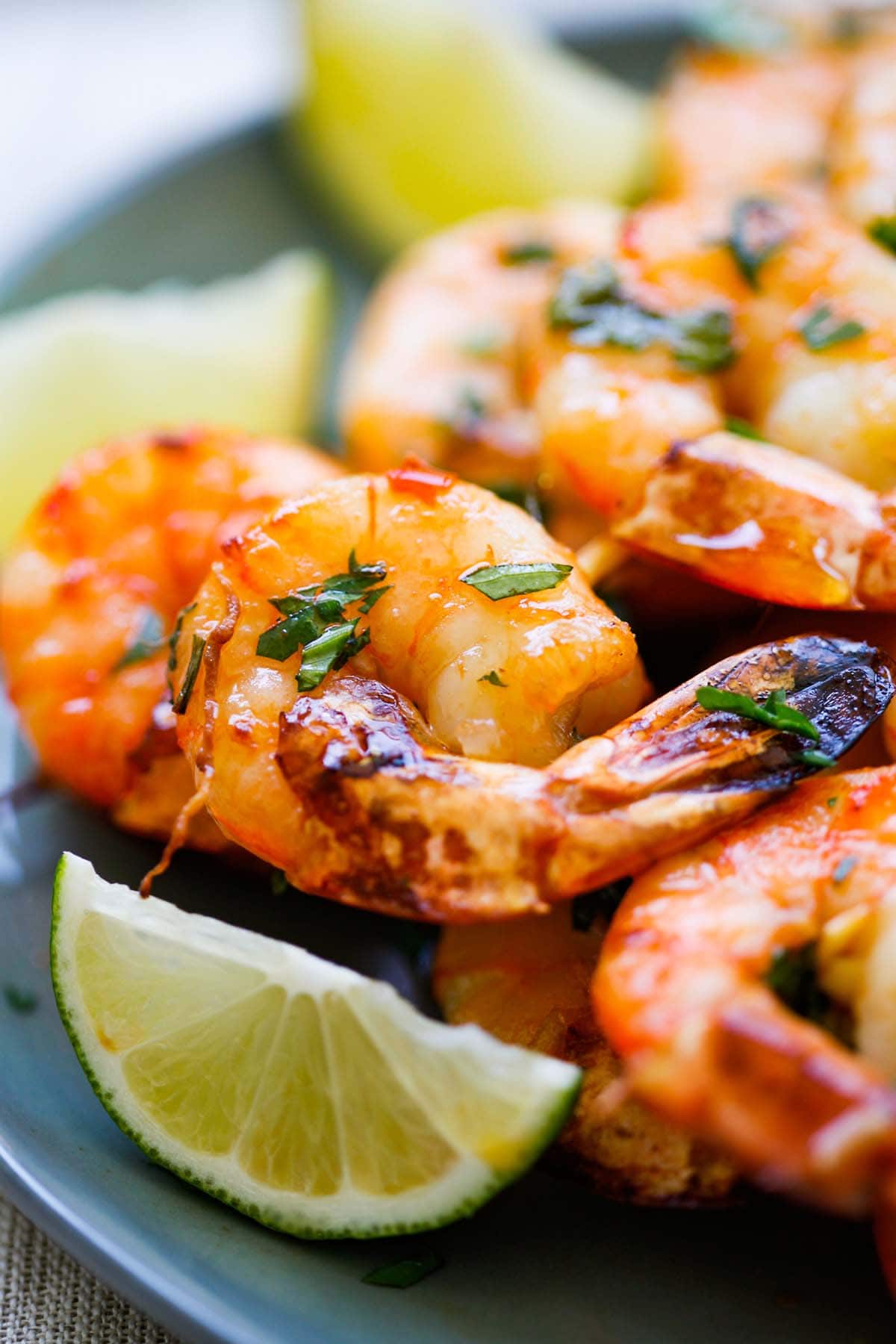 Close up shot of a shrimp coated with honey Sriracha butter and lime wedges on the side. 