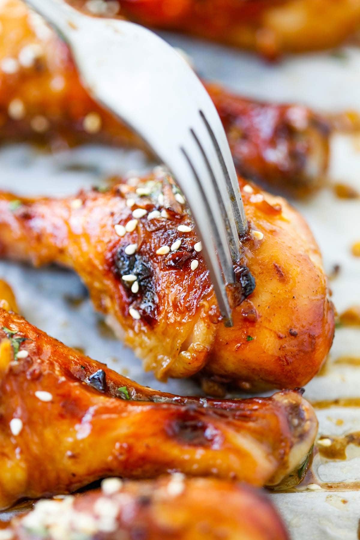 A fork piercing through a golden brown glazed chicken drumstick coated with hoisin sauce. 