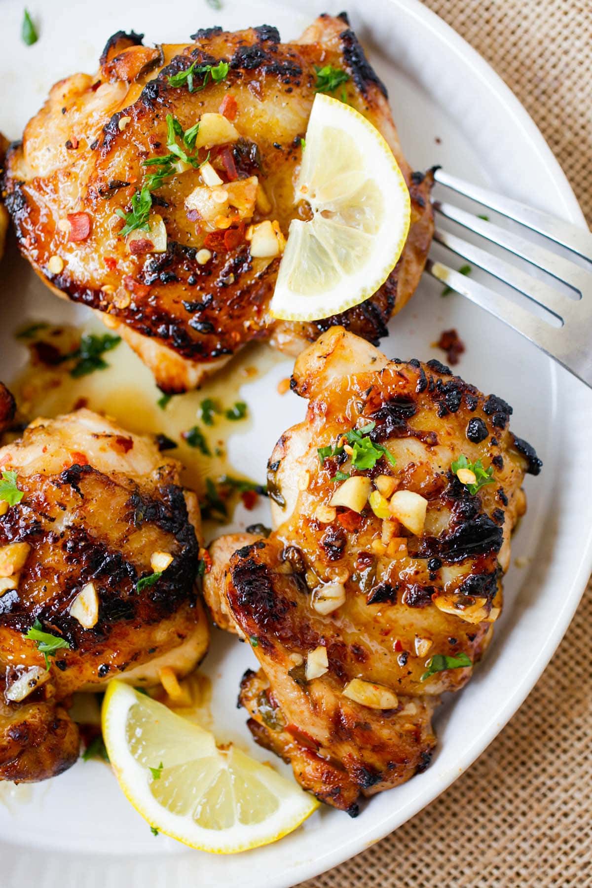 Chicken thigh with golden-brown exterior covered in citrusy lemon and savory garlic sauce served on a plate with fork on the side. 