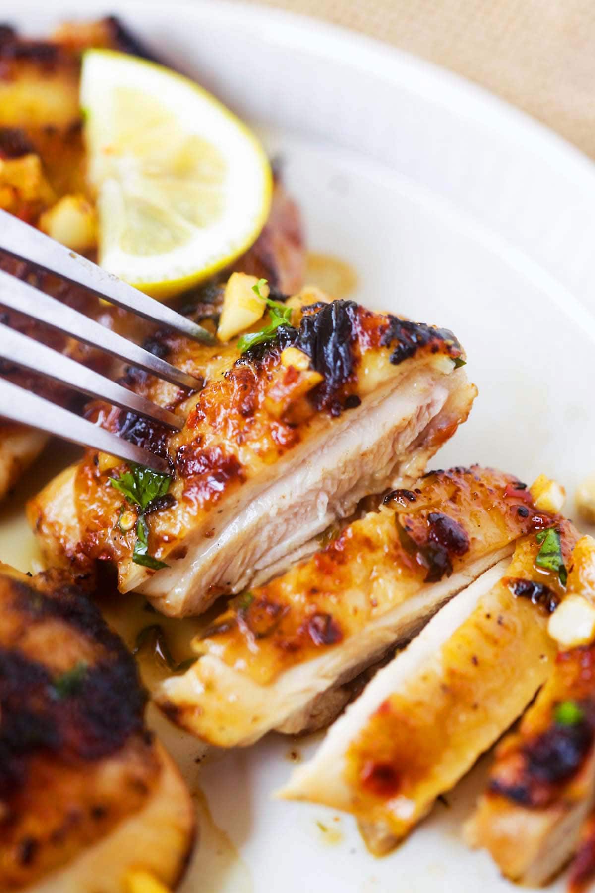 A fork piercing through a slice of tender and juicy garlic lemon chicken. 