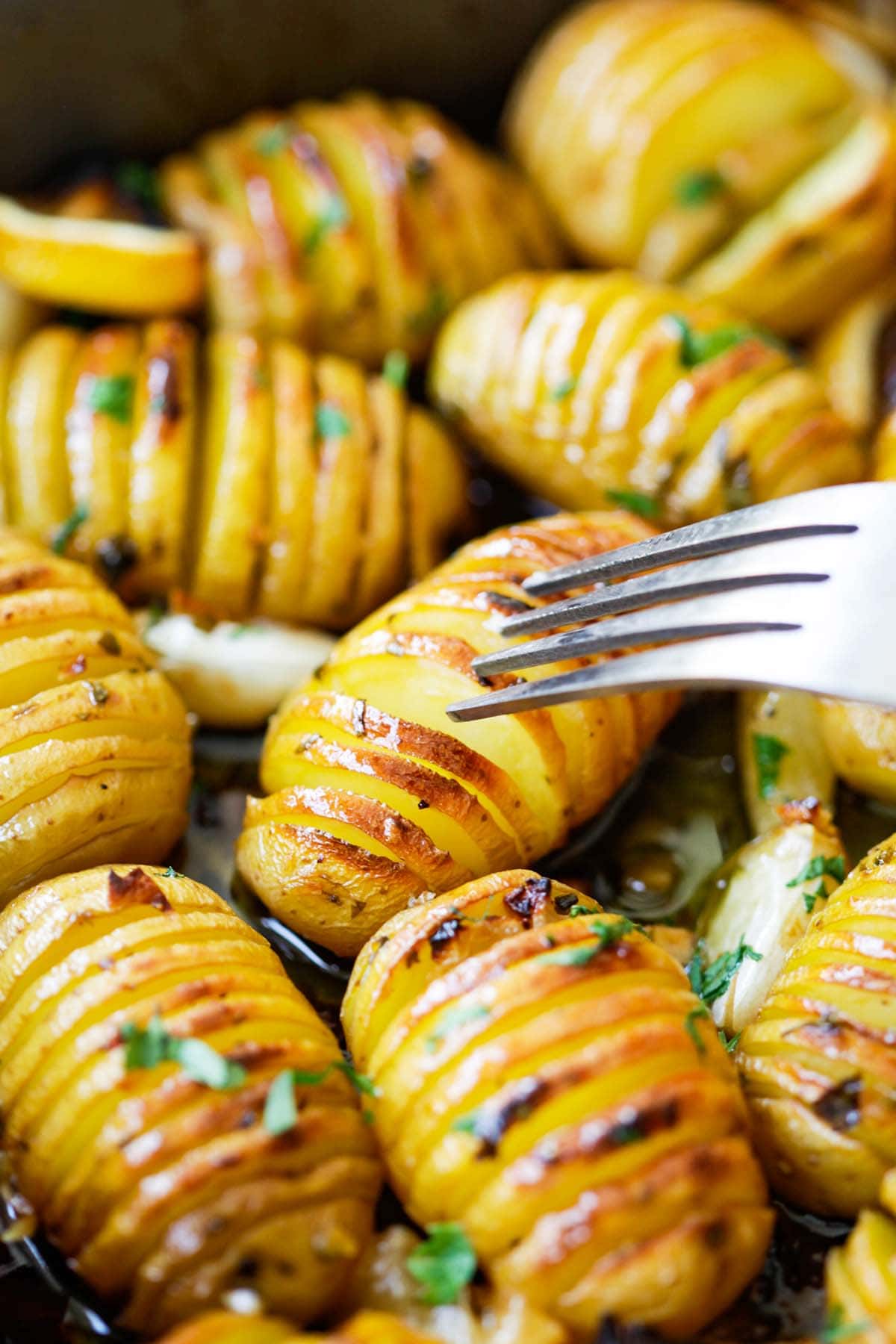 A fork delicately piercing through  oven-roasted golden-brown crust potatoes coated with lemon, garlic, and herbs.