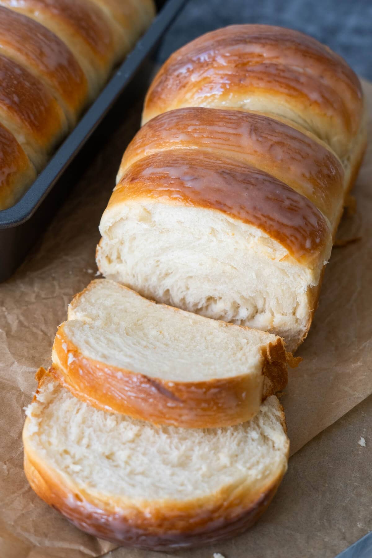 Soft fluffy bread roll coated with condensed milk on the outside laid on top of brown baking paper. 