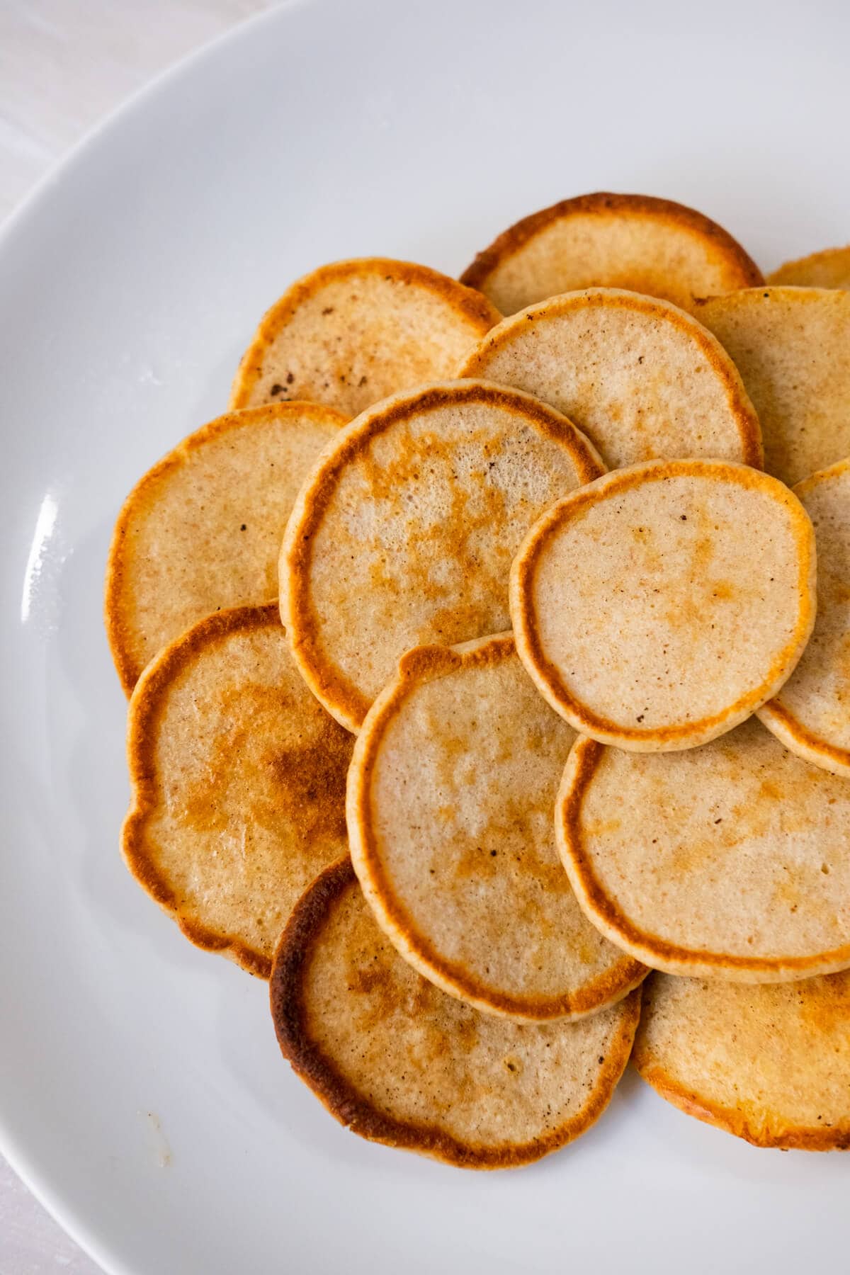 A plate of golden-brown blinis served on a white plate. 