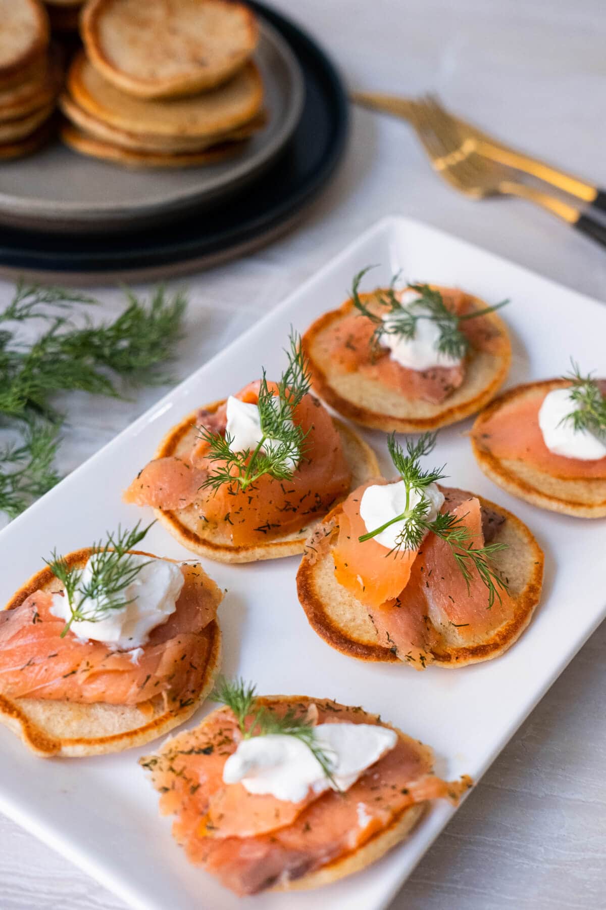 A close-up shot of a plate featuring a tempting display of golden-brown small Russian pancakes with a sour cream, smoked salmon, and fresh dill topped on top.