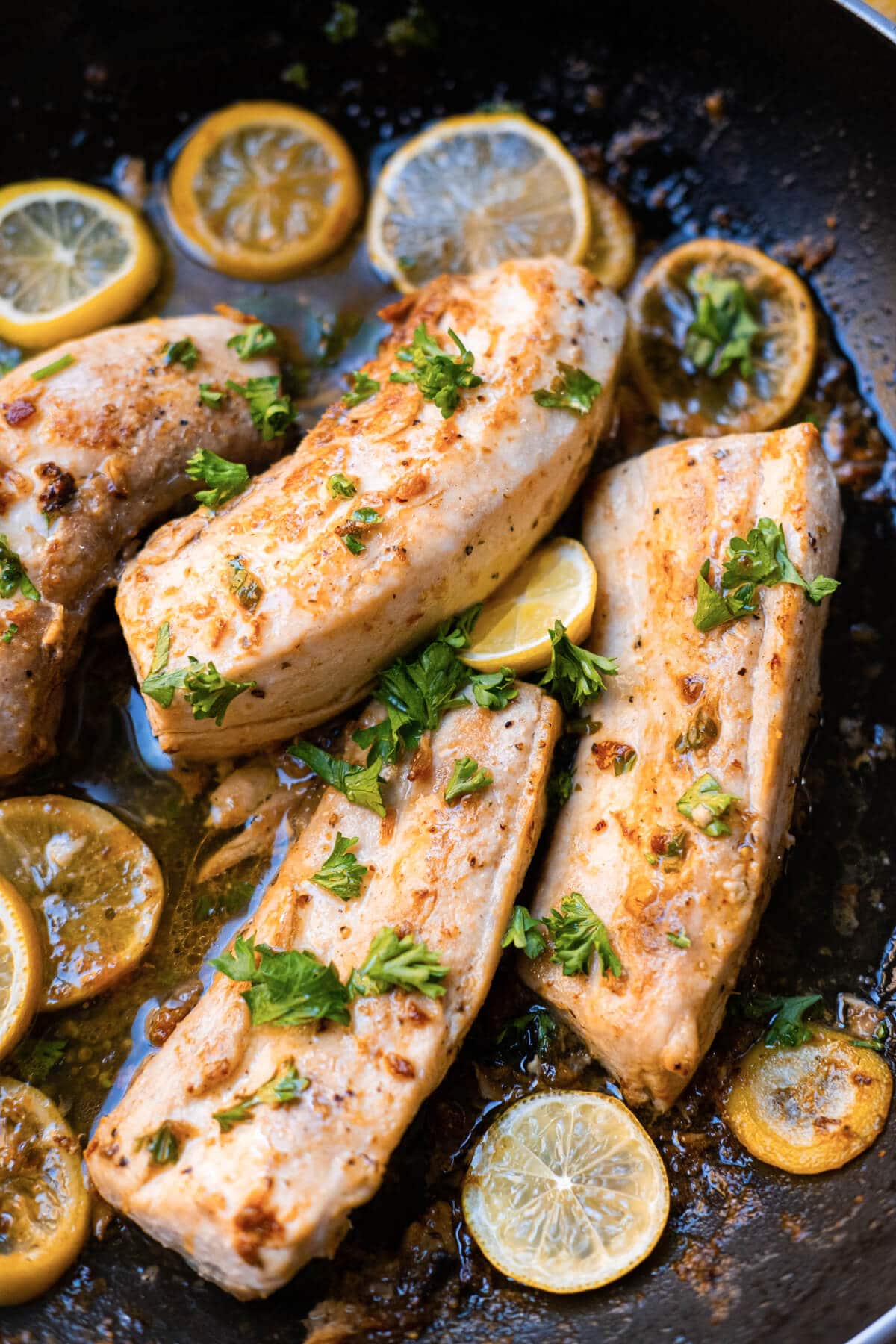 Beautifully seared mahi-mahi fillets generously coated in a rich and savory garlic butter sauce in a pan with lemon slices on the side and fresh parsley sprinkled on top. 