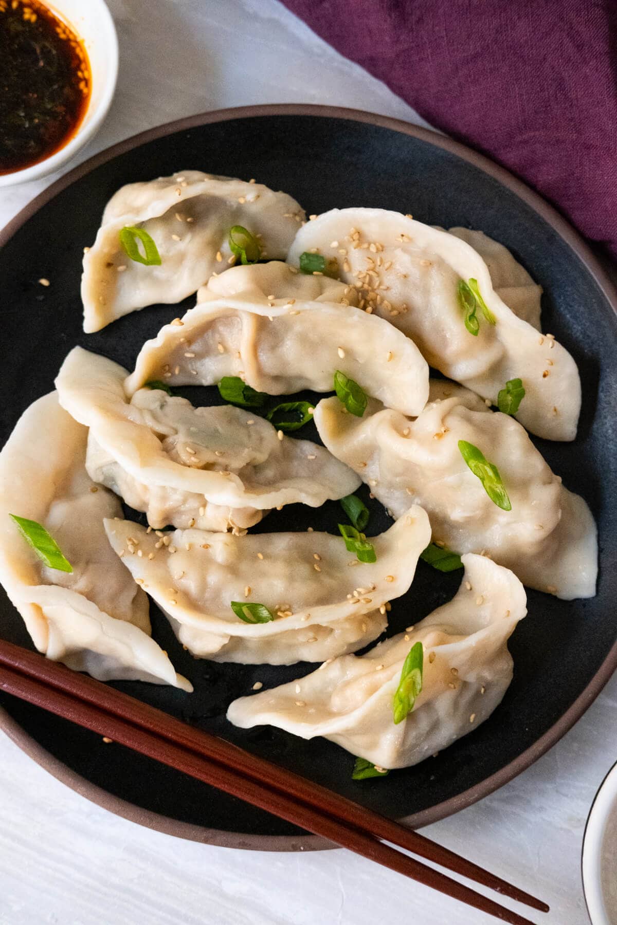 A plate of eight white Chinese dumplings served on a black plate with chopsticks on the side. 