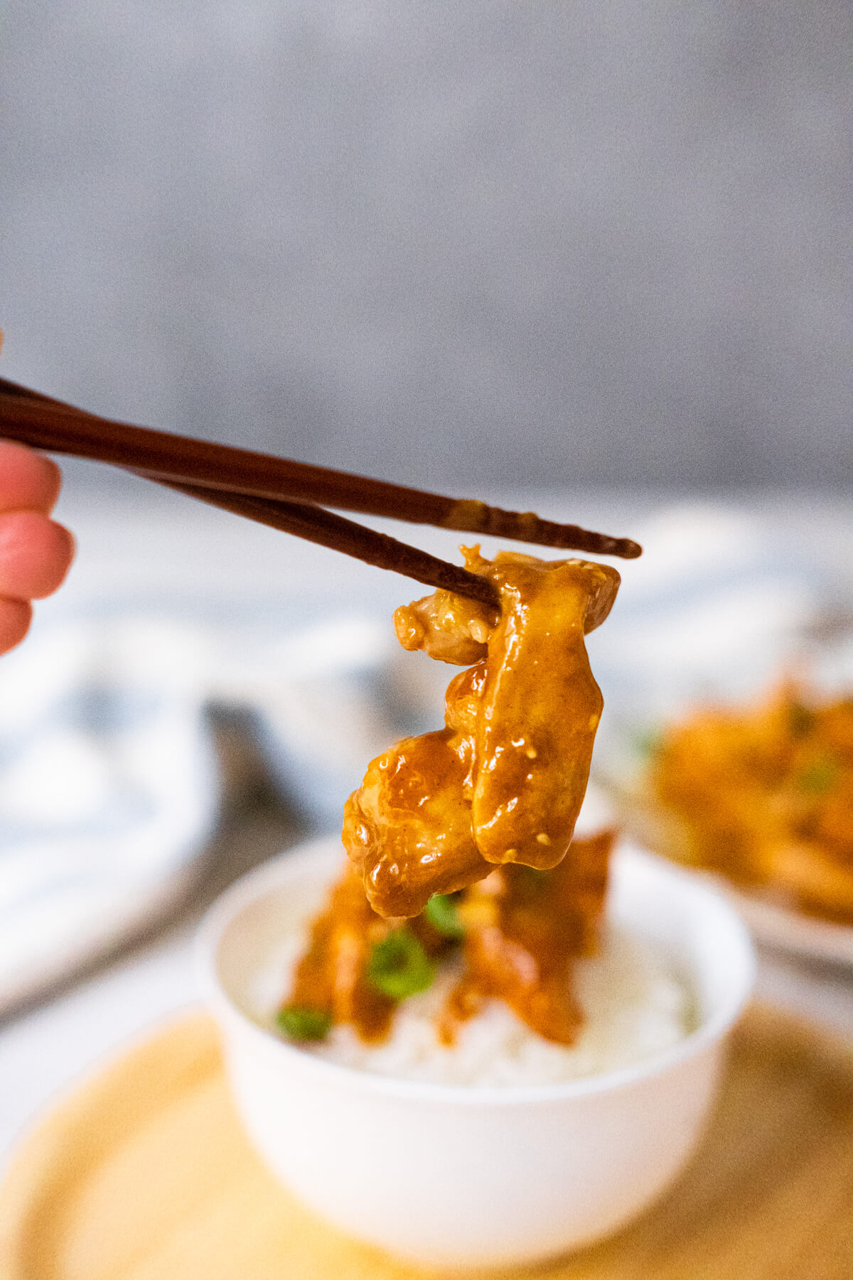 A chopstick holding up a piece of orange bourbon sauce coated flavorful chicken strip. 