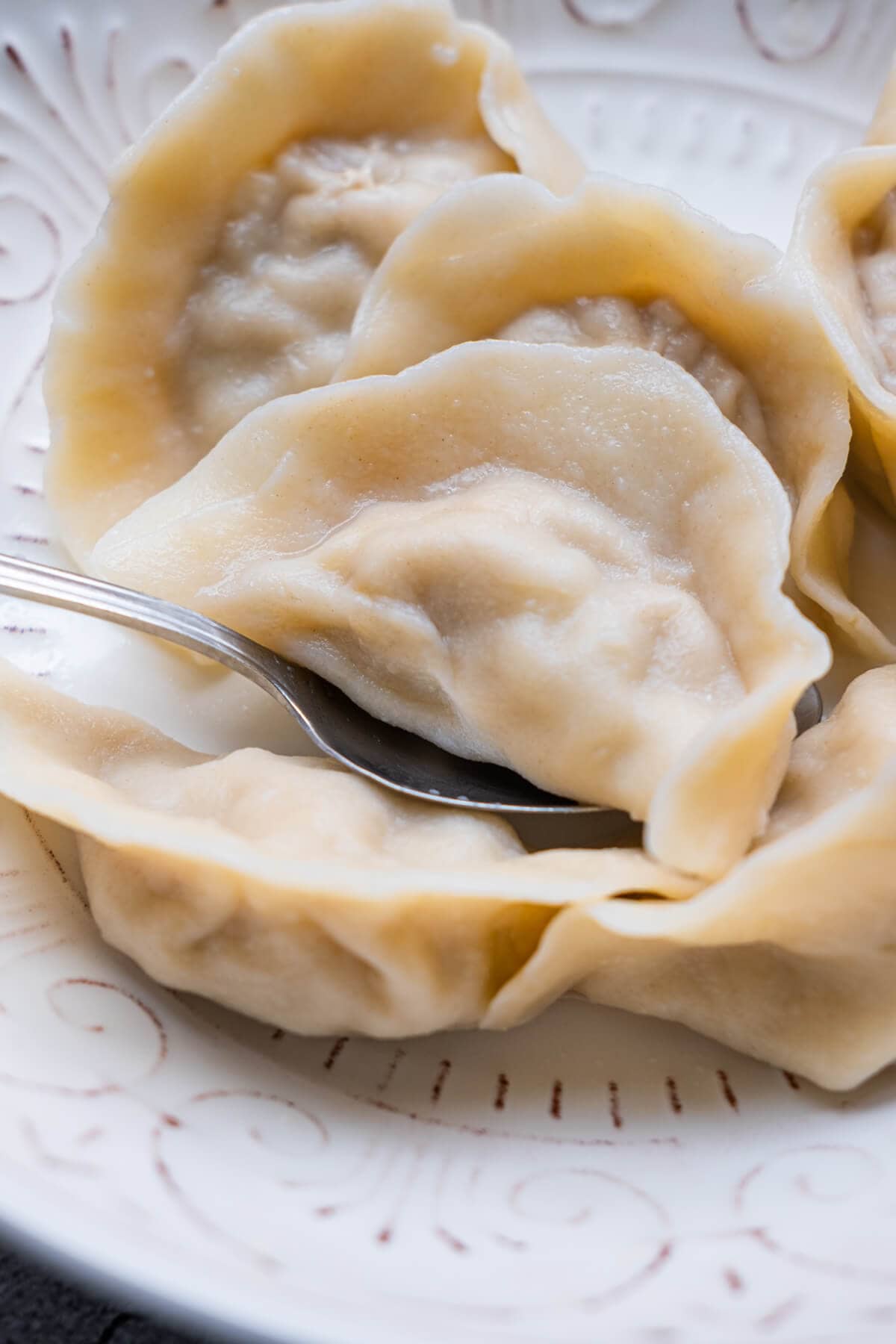 A spoon scooping up a dumpling from a plate of dumplings. 