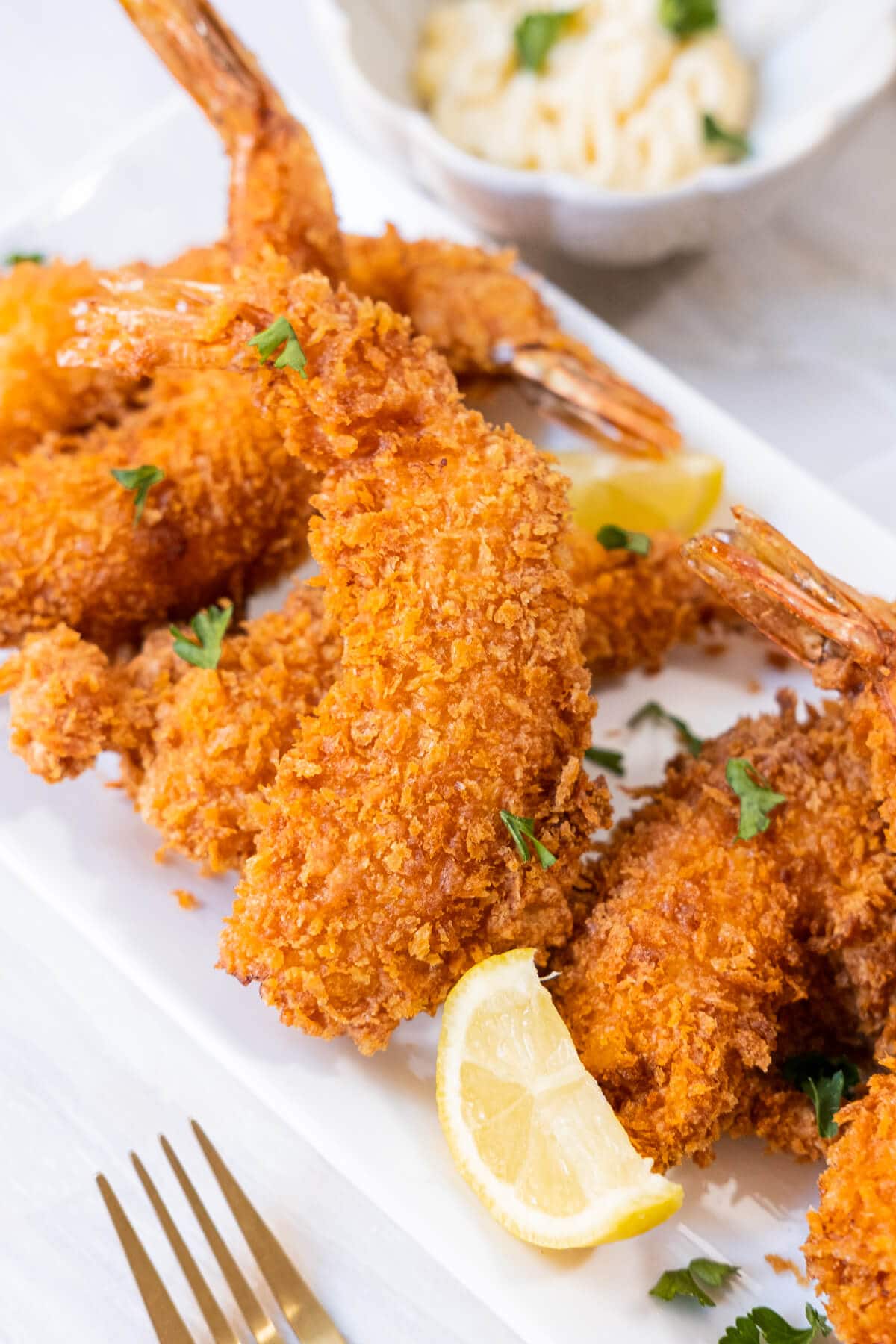 Thick breaded crust shrimps served on a long rectangular white plate with lemon wedges. 
