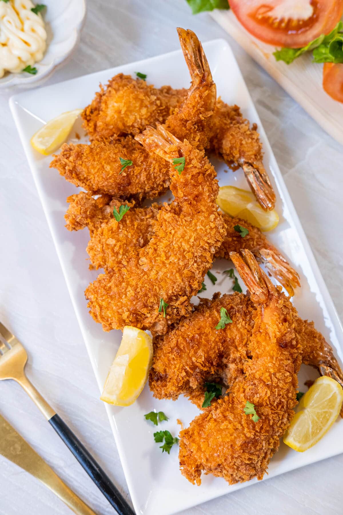 Six golden-fried shrimp on a white platter next to lemon wedges.