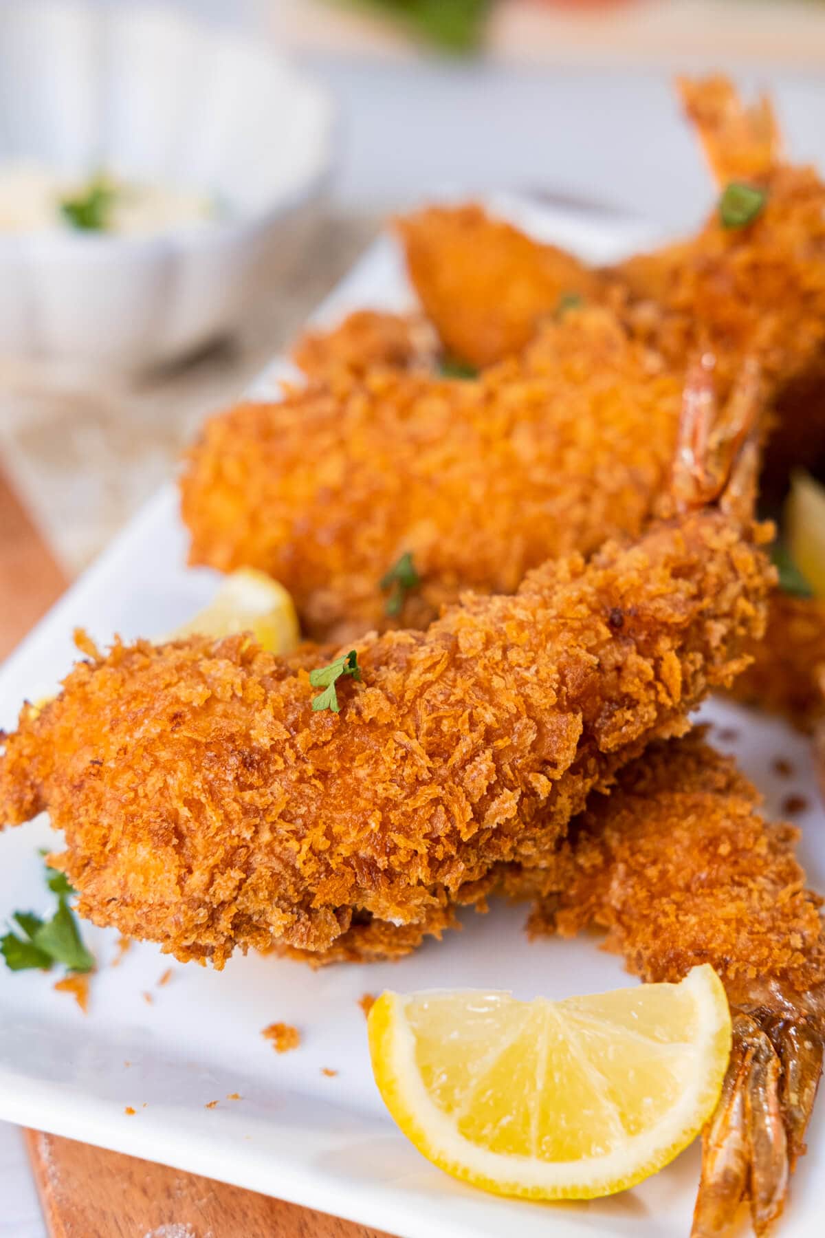 A close up shot of crispy golden brown fried shrimp with lemon wedges on a plate. 