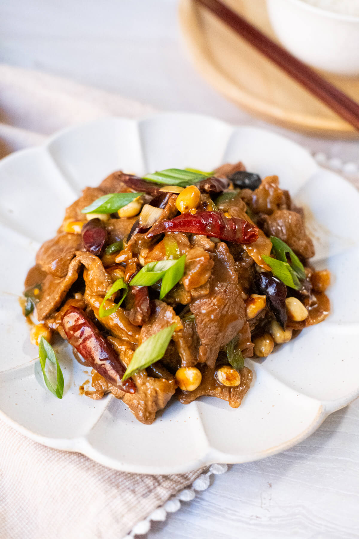 Tender beef with roasted peanuts and vegetables covered in spicy Kung Pao sauce served on a white plate. 