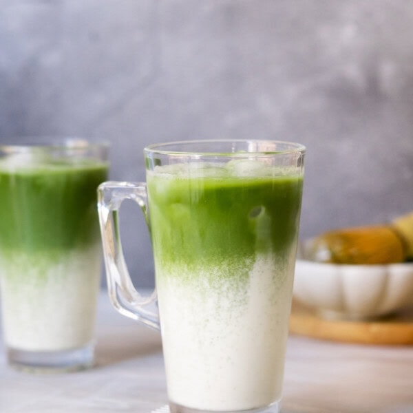 Two iced Matcha latte with a small plate in the back.