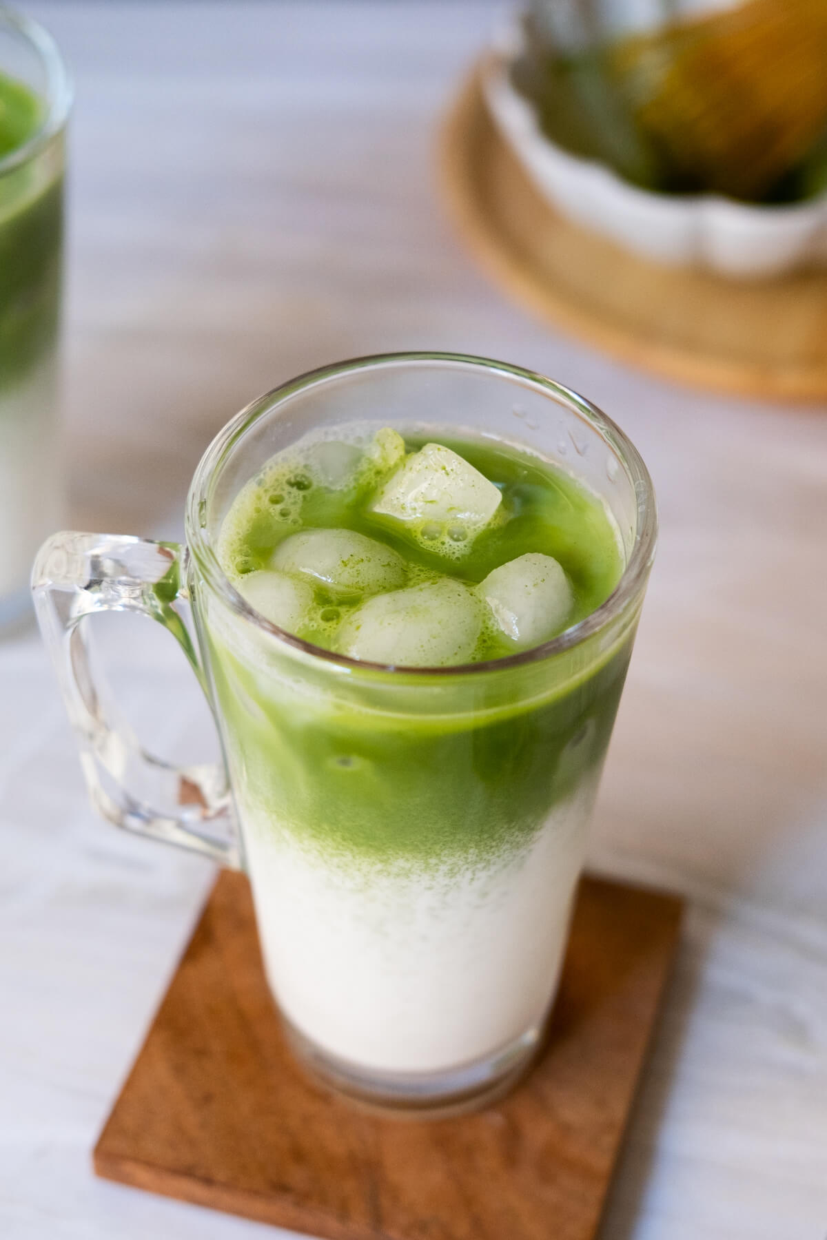 Two glasses of iced matcha latte, with ice cubes.