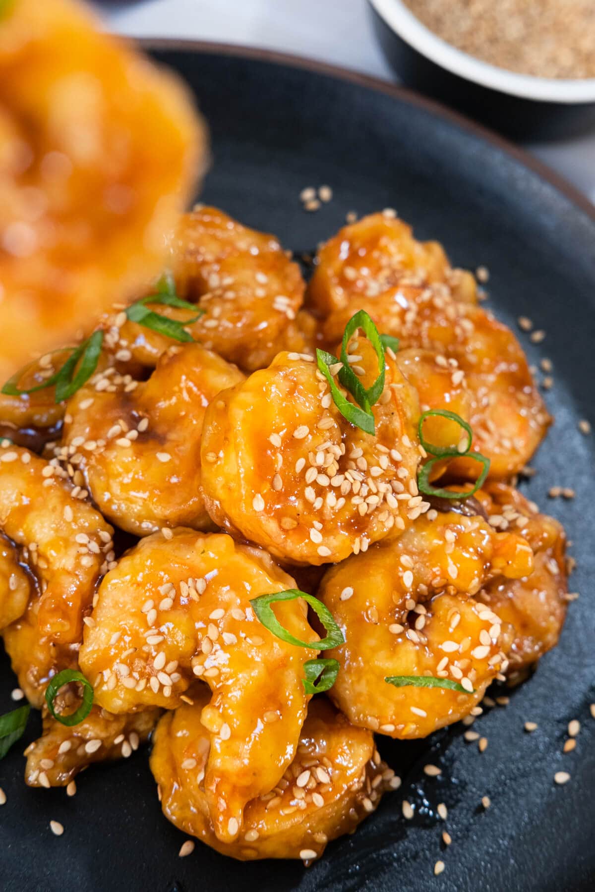 Close up of shrimps coated in a sweet and savory sauce garnished with white sesame seeds.