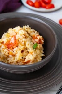 Spanish Rice in a black bowl and placed on a plate and with a dish of fresh tomatoes placed behind.