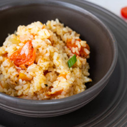 Spanish Rice in a black bowl and placed on a plate and with a dish of fresh tomatoes placed behind.