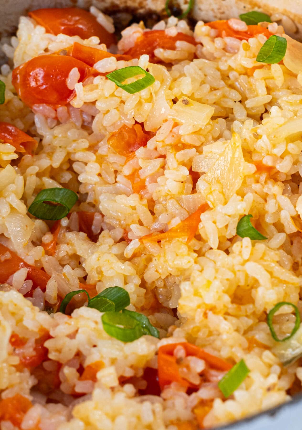 A close up shot of fluffy golden short grain rice mixed with tomato, garlic, onion, and bay leaves.  