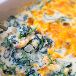 Creamed spinach in a baking dish scooped by a spoon.