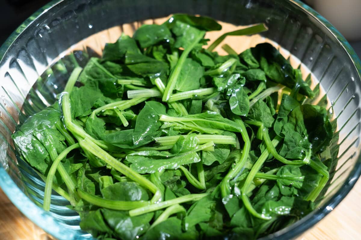 Boiled spinach sit in a bowl of cold water.