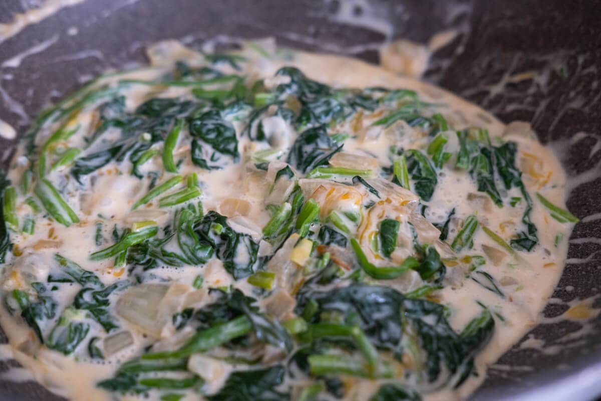 Creamed spinach with melted cheese and onion in a skillet.