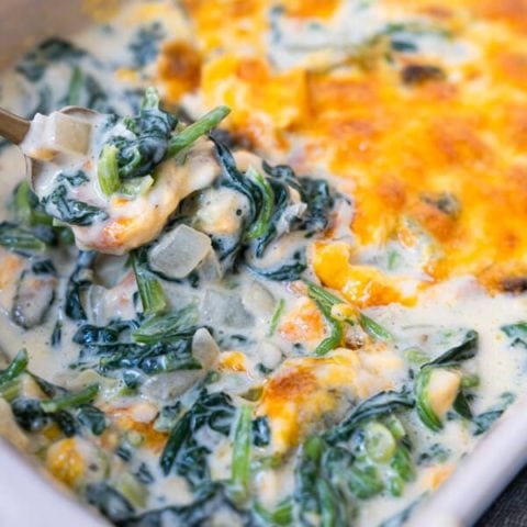 Creamed spinach with baked cheese on top in a baking dish.