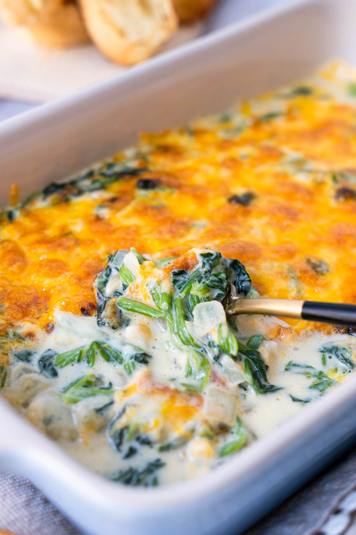 Spinach loaded with cheese flavor and creamy sauce in the baking dish with some bread next to it.