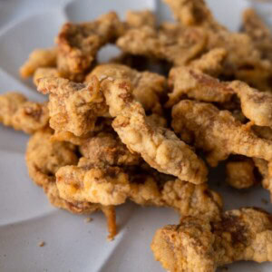 Crispy fried pork shoulder strips on a white plate.