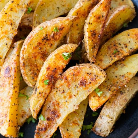 Crispy baked garlic parmesan potato wedges with chopped parsley sprinkled on top.