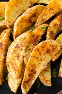 Golden crispy garlic parmesan potato wedges with chopped parsley on top.