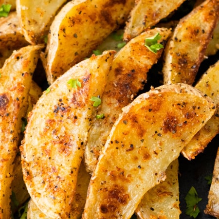 Golden crispy garlic parmesan potato wedges with chopped parsley on top.