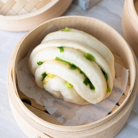 One scallion bun in a parchment lined bamboo steamer.