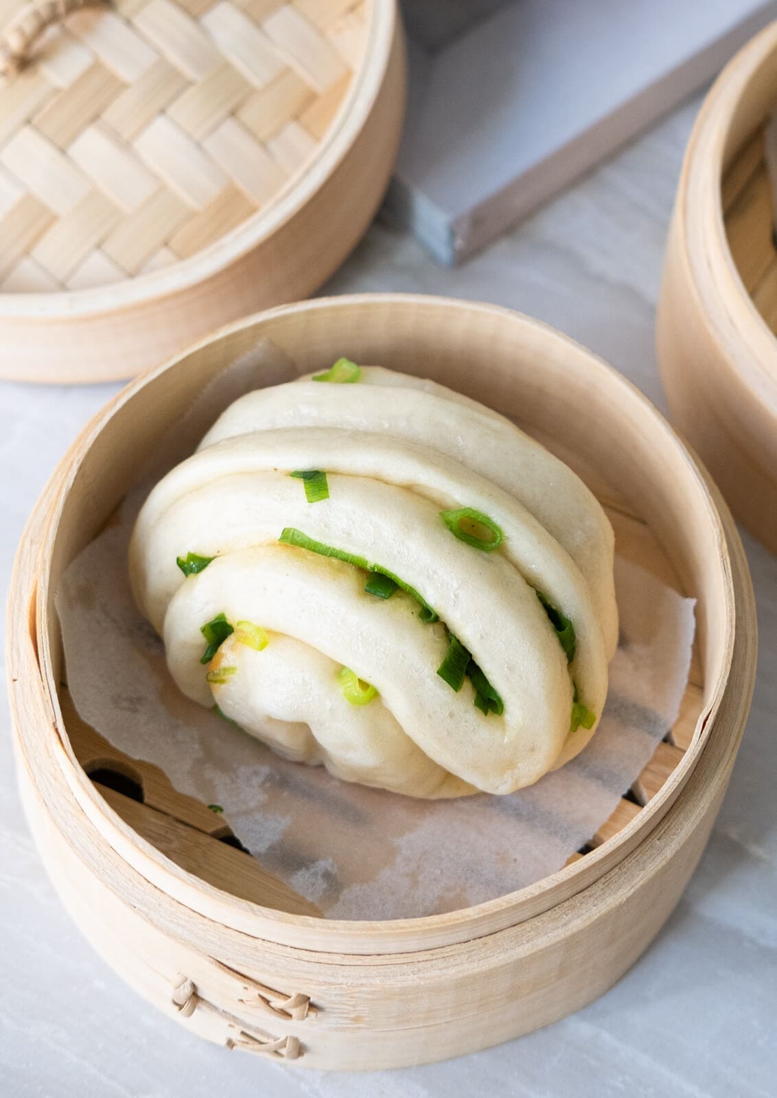 One steamed scallion bun placed on a wooden steamer with a book placed next to it.