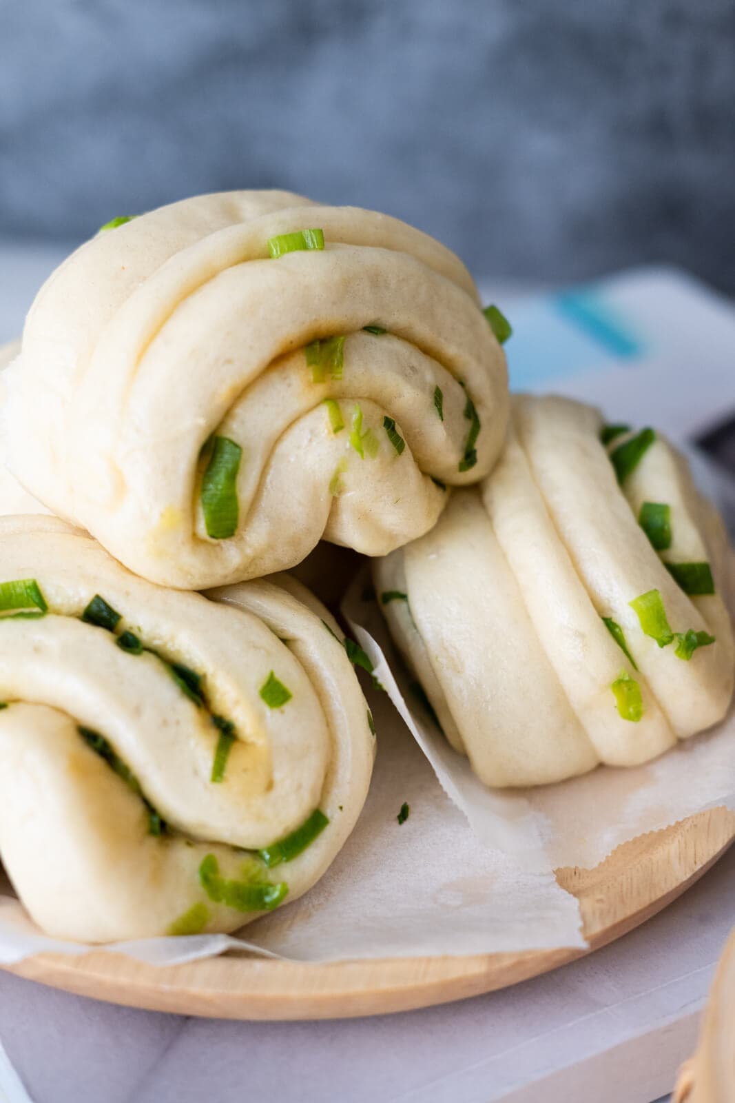 Three scallion buns stack on each other and placed on a parchment lined wooden plate.
