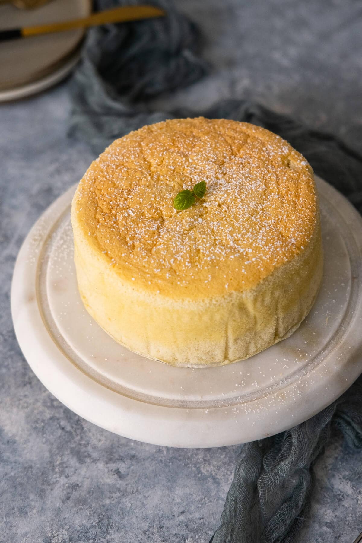 Yogurt cake on a marble stand with two small plates placed behind it. 