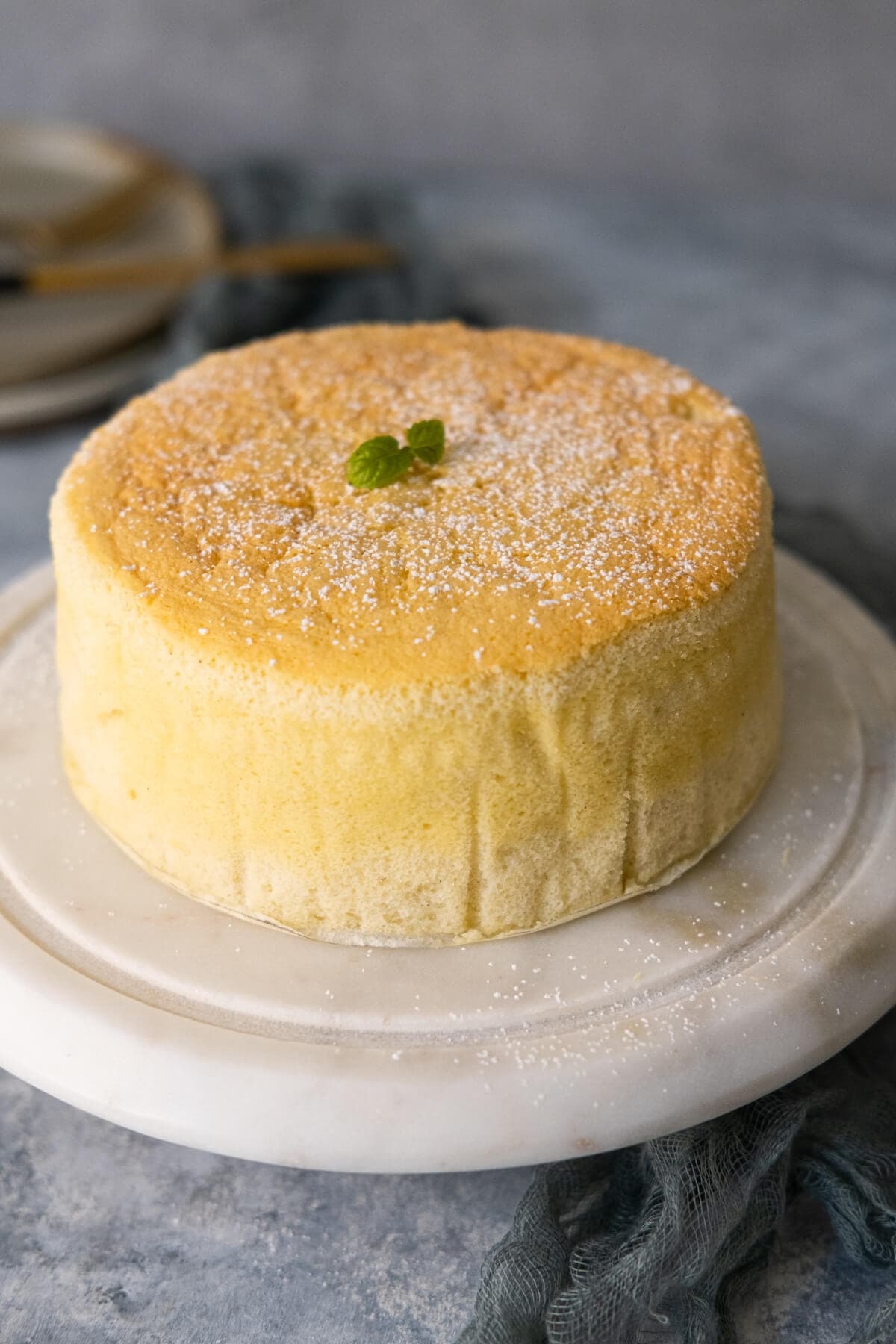 Yellow cake placed on a white marble stand with mint leaves on top. 