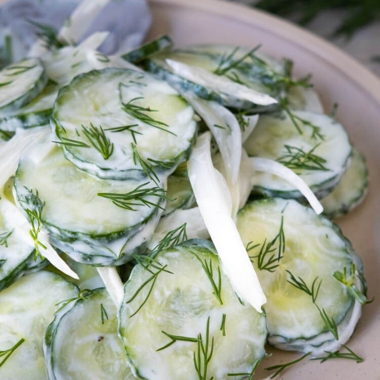 Creamy cucumber salad with white onion slices and fresh chopped dill on top.